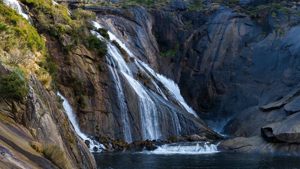 A waterfall cascading down a rocky cliff into a pool below.
