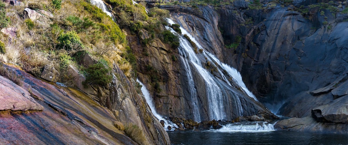 A waterfall cascading down a rocky cliff into a pool below.