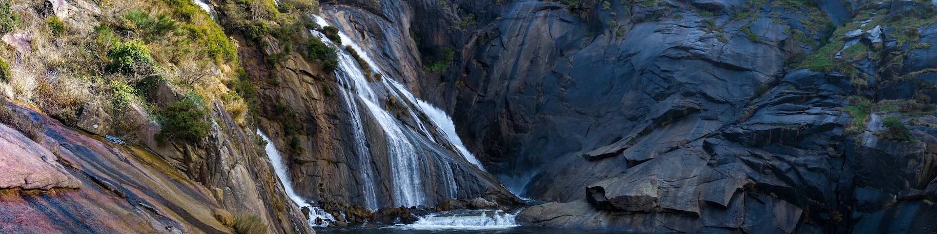 A waterfall cascading down a rocky cliff into a pool below.