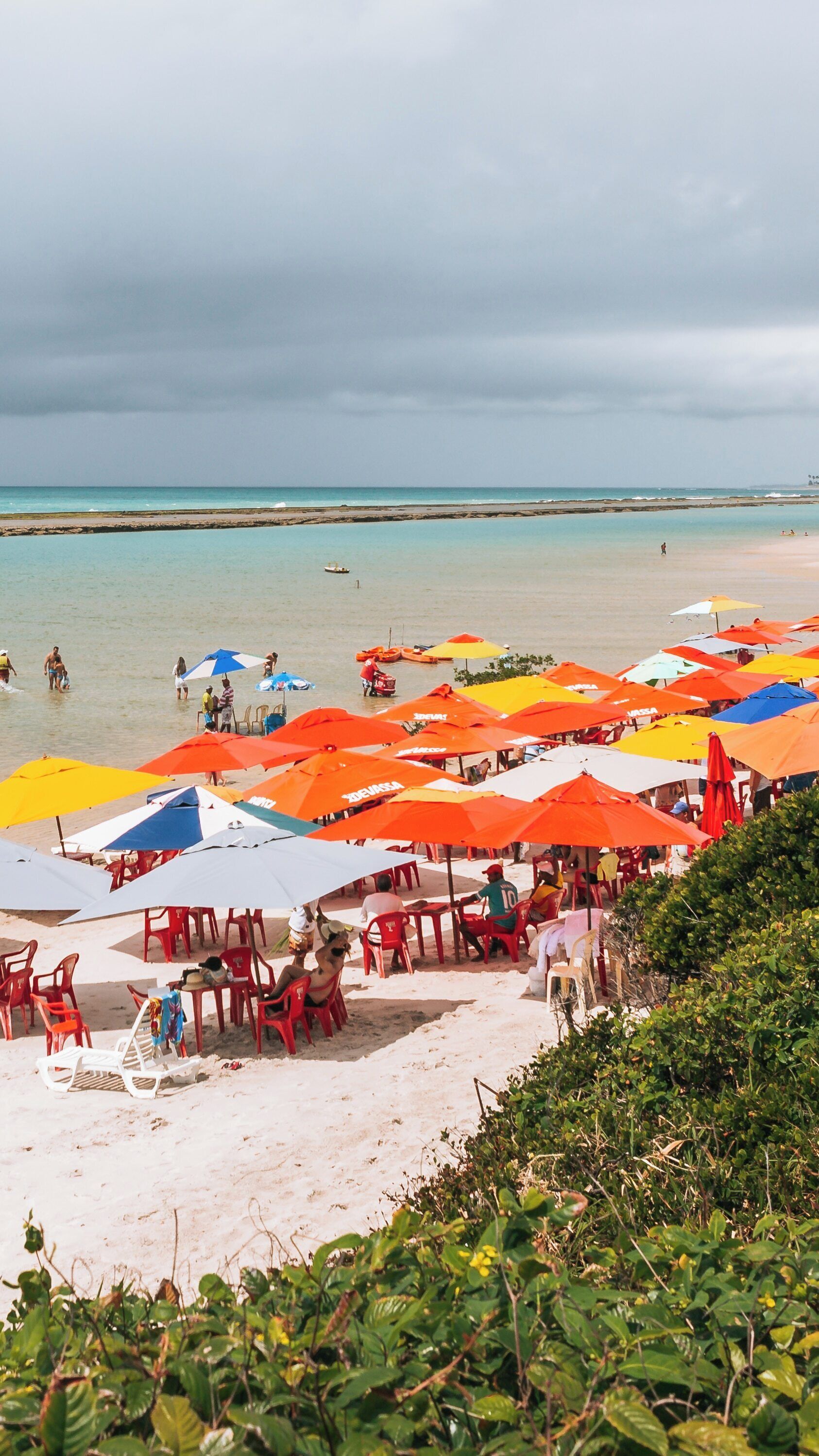 Colorful umbrellas dot the sandy shore of Muro Alto Beach in Porto de Galinhas, inviting relaxation and leisure under the cloudy sky