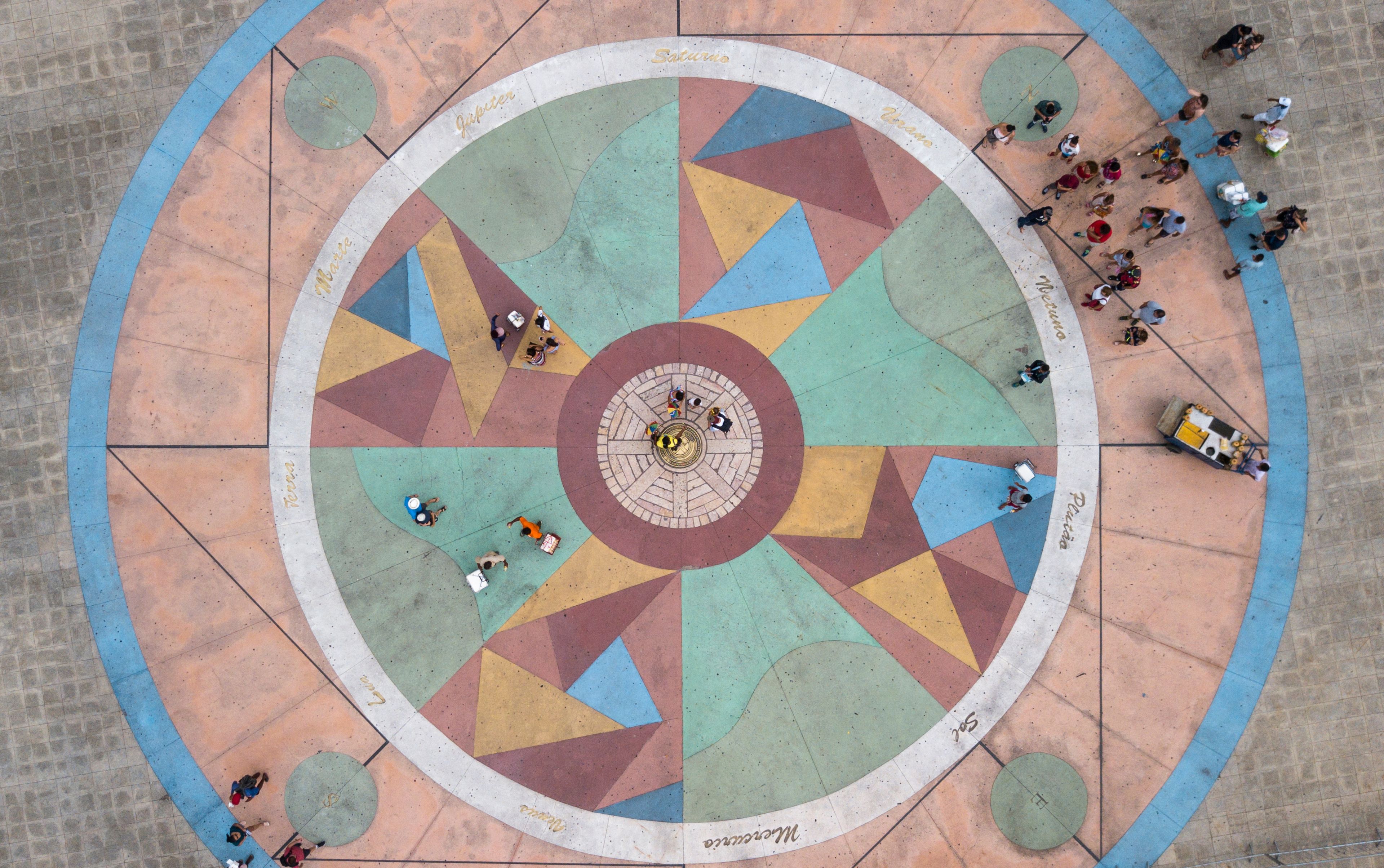 A colorful circular plaza with geometric patterns and people walking around.