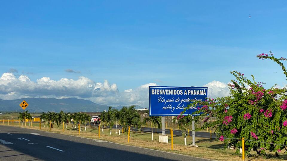 A road with a blue sign reading "BIENVENIDOS A PANAMÁ" and a mountain range in the background.