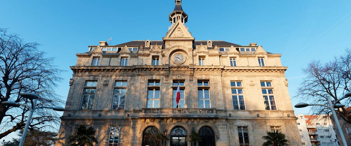 A large, historic building with a clock tower, arched windows, and a flag.