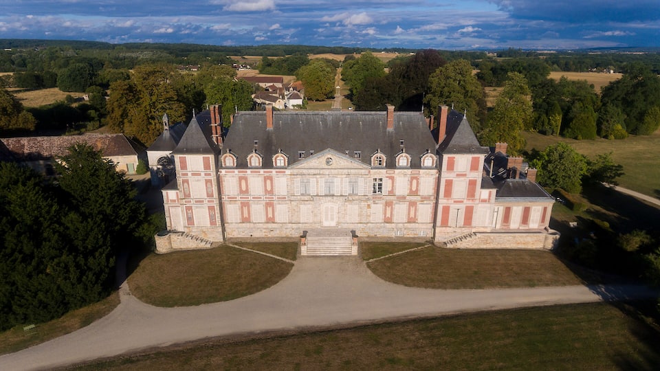 A large, historic building with a symmetrical facade, central entrance, and a formal garden.