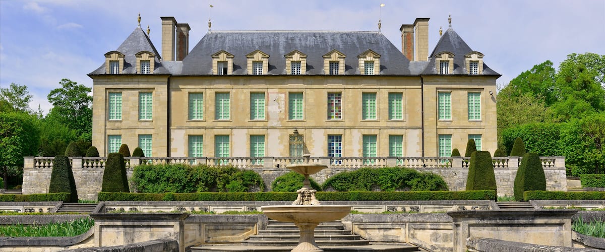 A large, historic building with a symmetrical facade, multiple chimneys, and a central fountain.