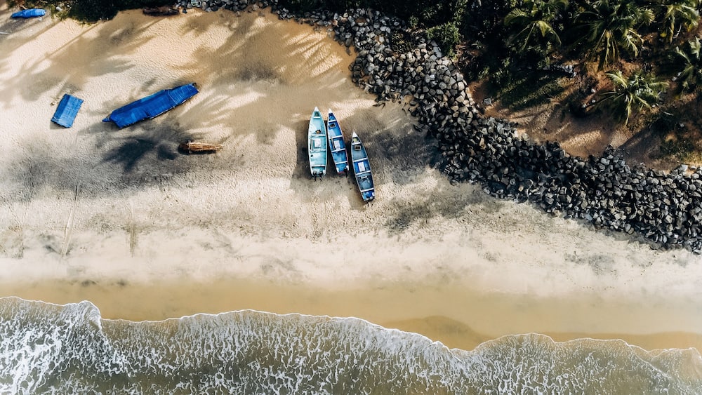 Ein sandiger Strand mit Booten, Palmen und einer felsigen Küstenlinie.