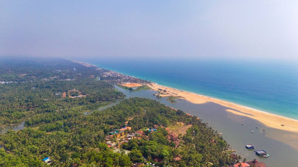 A coastal landscape with a beach, a river, and dense greenery.