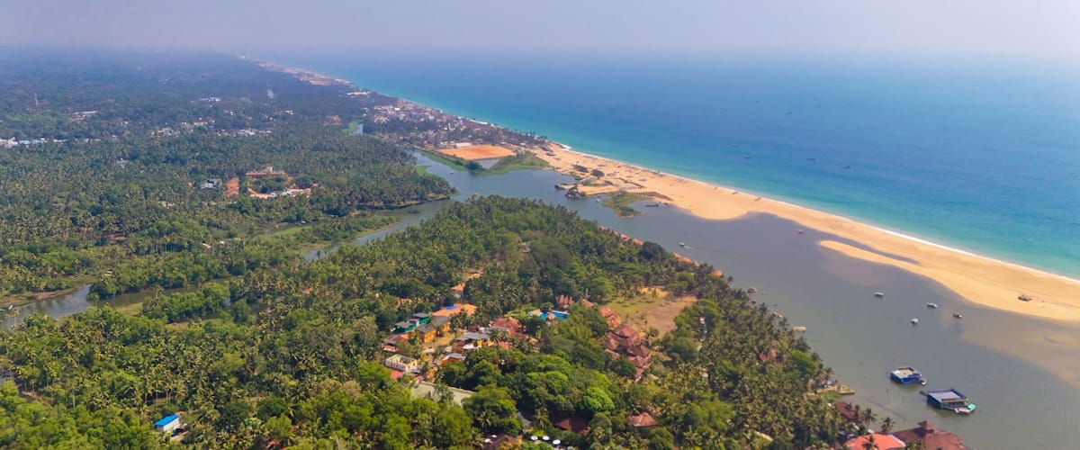 A coastal landscape with a beach, a river, and dense greenery.