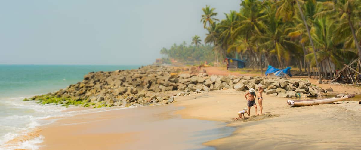 A family of 2 parents and a girl are relaxing on a empty tropical beach in the Kerala state, India.