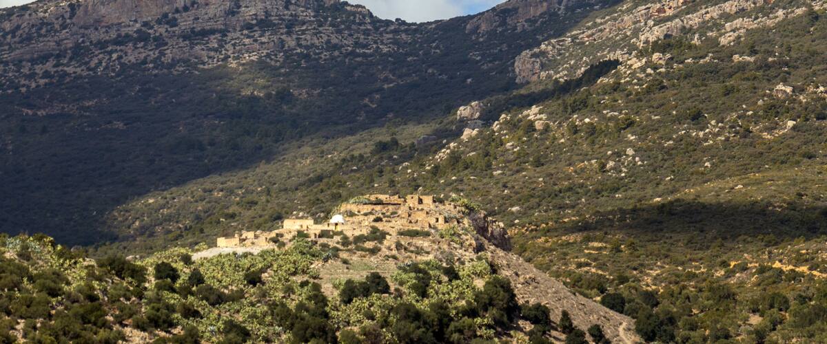A mountainous landscape with a small village nestled among rocky hills and sparse vegetation.