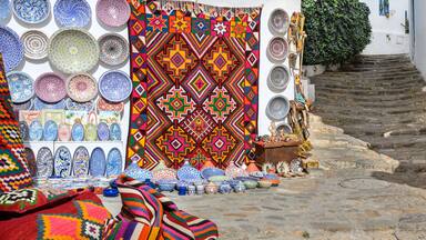 A narrow stone staircase leading up to a white building with colorful textiles and ceramics displayed outside.
