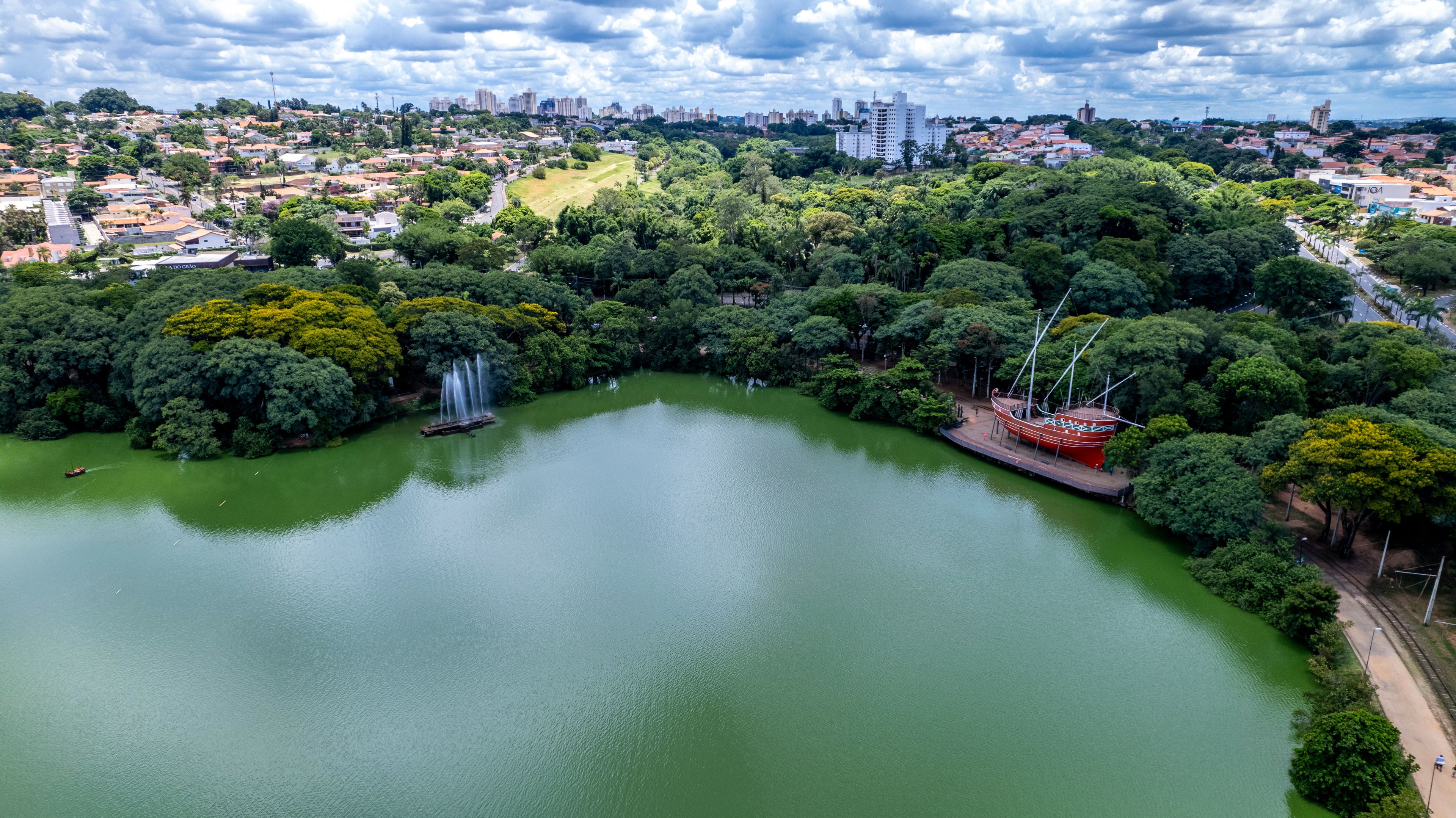 A large green lake surrounded by dense trees and a cityscape in the background.