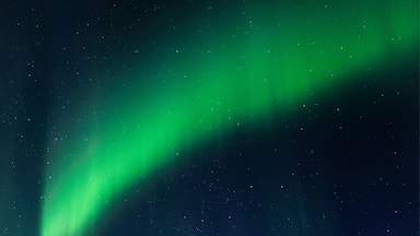 The Northern Lights over a snowy landscape with a small cabin.