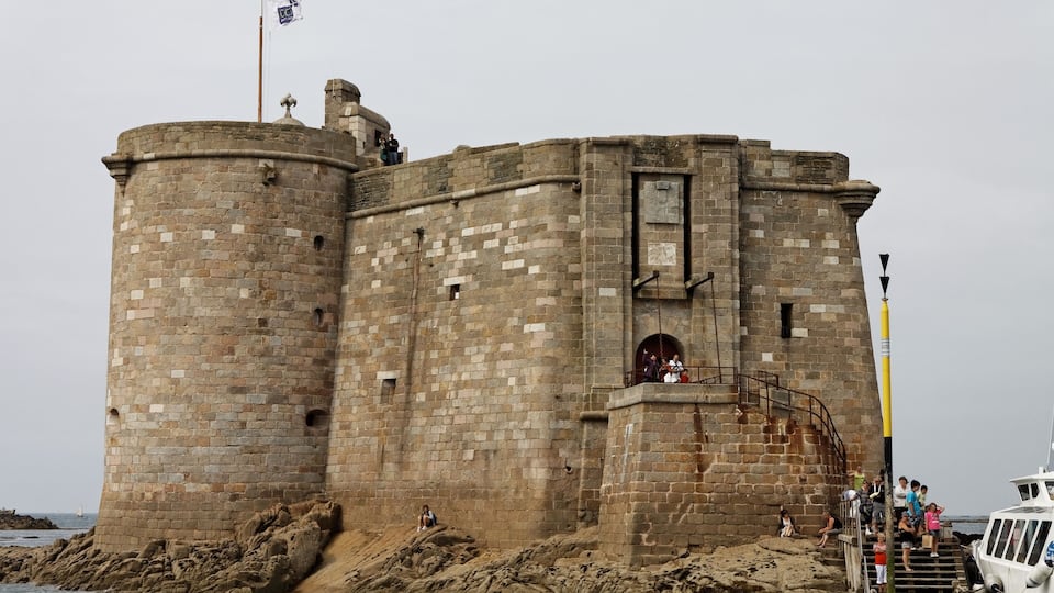 A historic stone castle with a flag on top, situated by the sea.