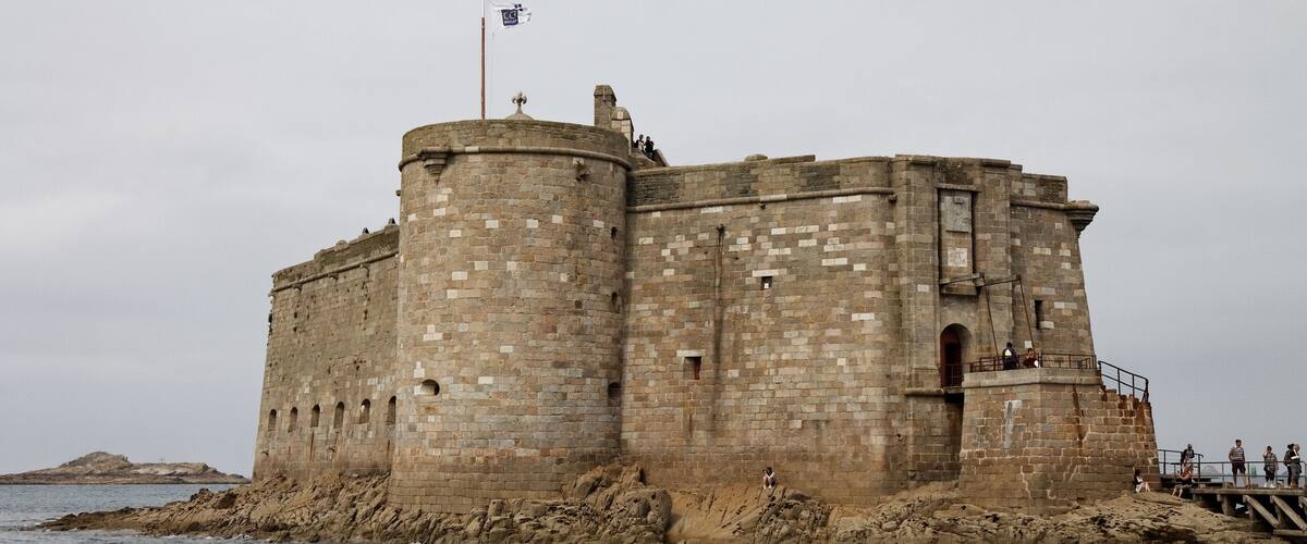 A large stone castle by the sea with a flag on top.