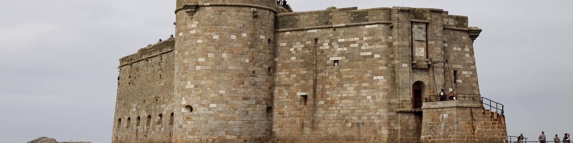 A large stone castle by the sea with a flag on top.