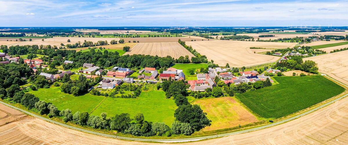 An aerial view of a rural village with houses, fields, and wind turbines in the distance.