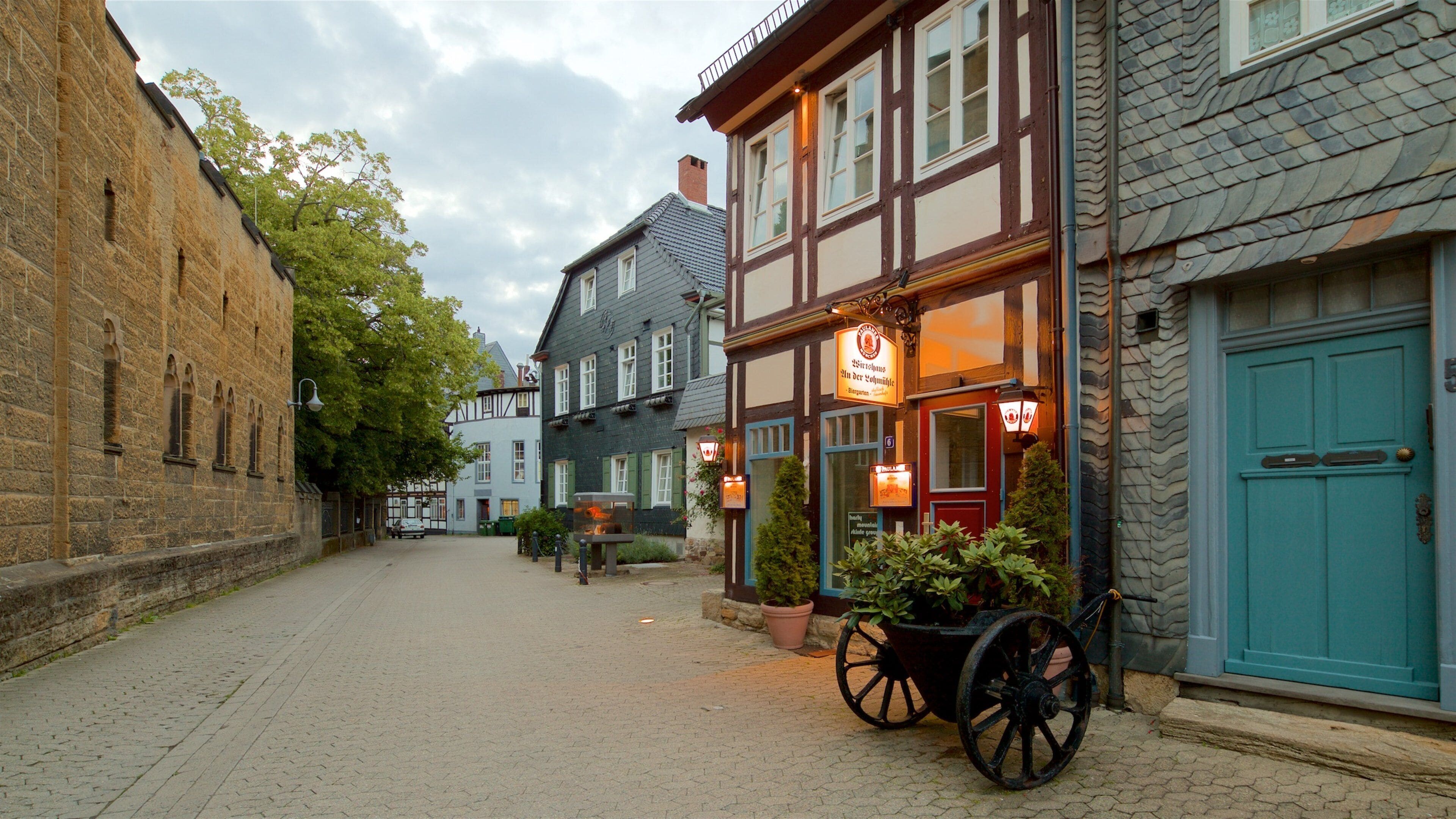 A cobblestone street lined with historic buildings, a horse-drawn cart, and potted plants.