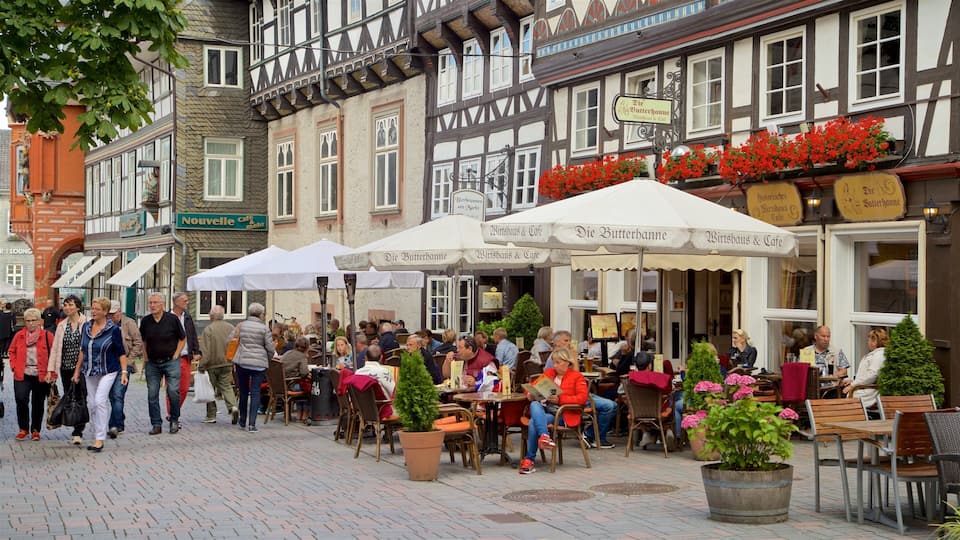 A bustling outdoor café area with traditional half-timbered buildings, outdoor seating, and red flowers.