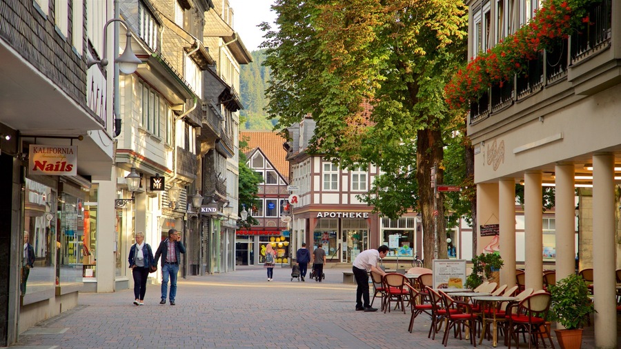 A cobblestone street lined with historic buildings, a café with outdoor seating, and pedestrians walking along.
