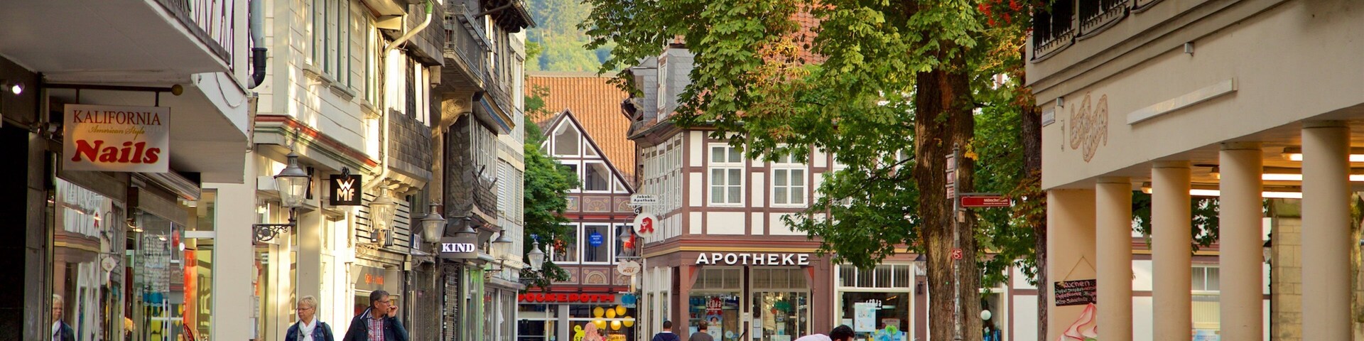 A cobblestone street lined with historic buildings, a café with outdoor seating, and pedestrians walking along.