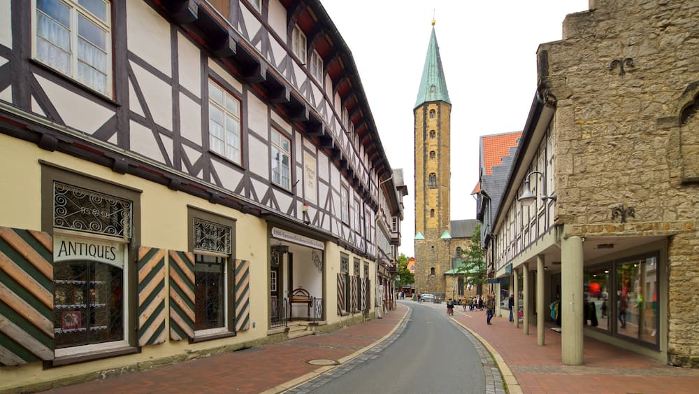 Une rue étroite bordée de maisons à colombages, avec le clocher d’une église en arrière-plan.