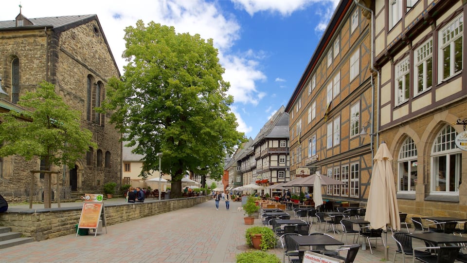 A cobblestone street lined with historic buildings, outdoor seating, and a large tree.