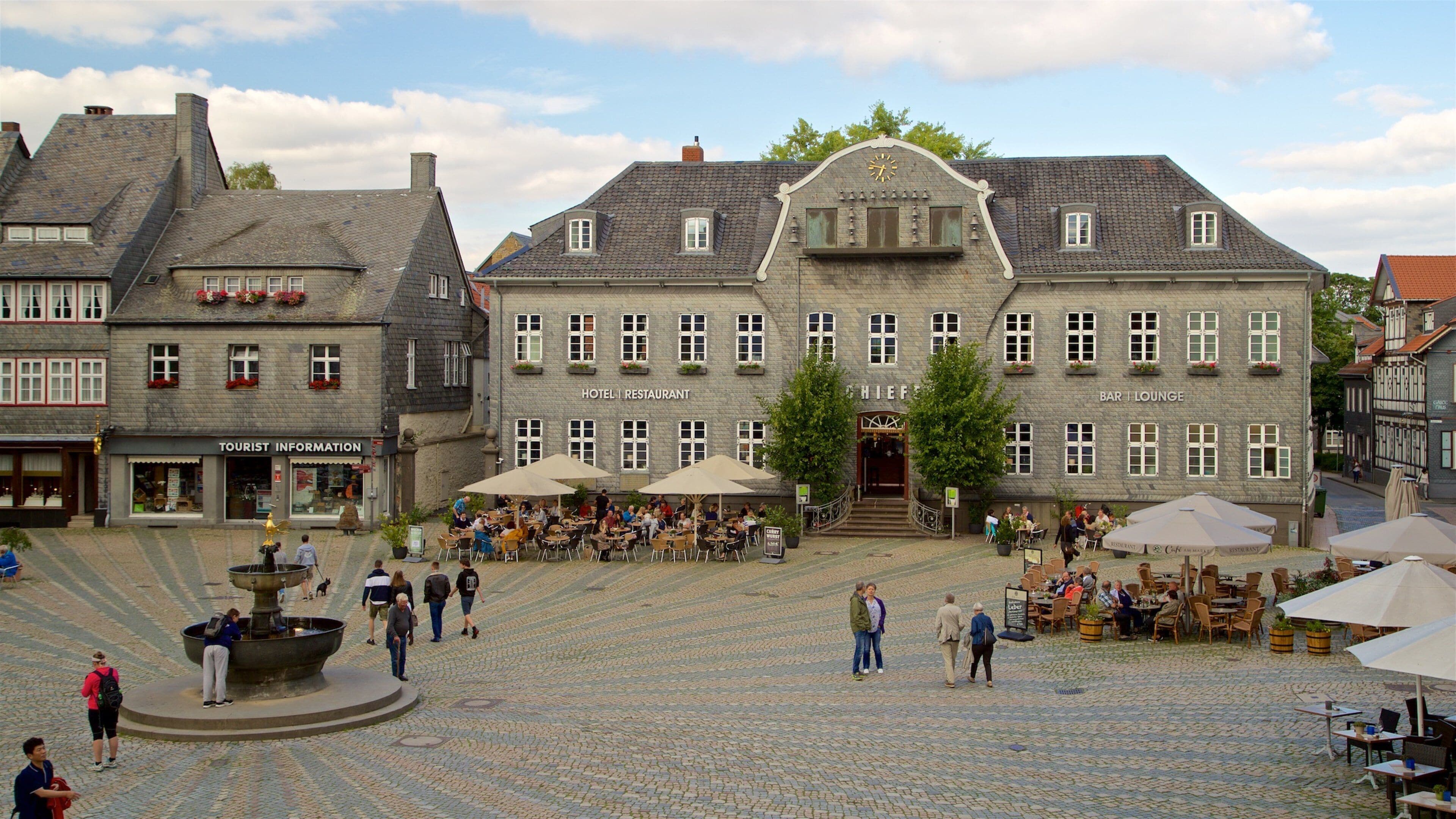 A cobblestone square with a fountain, historic buildings, and outdoor seating areas.