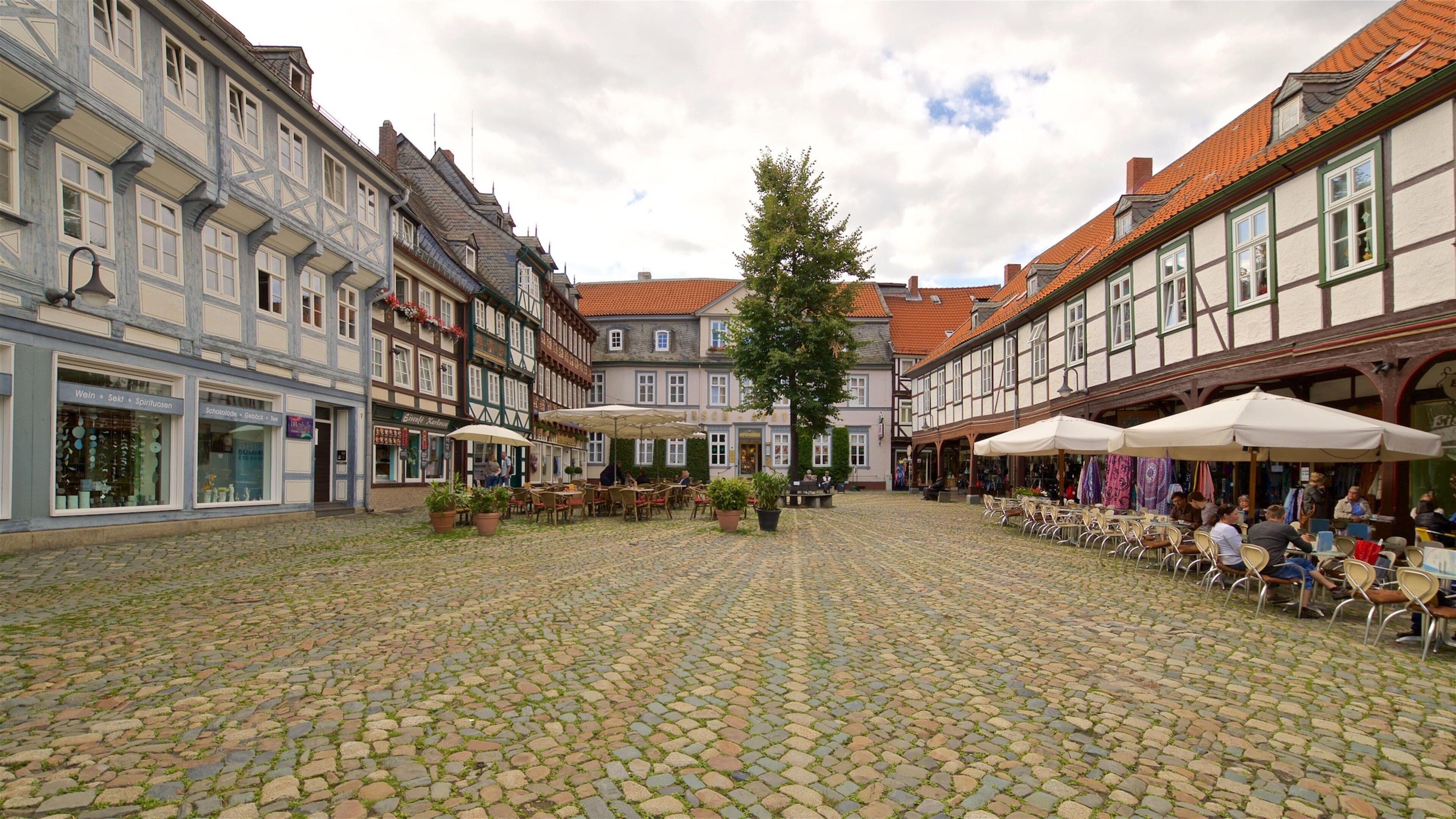 A cobblestone square with traditional European architecture, outdoor seating, and shops.