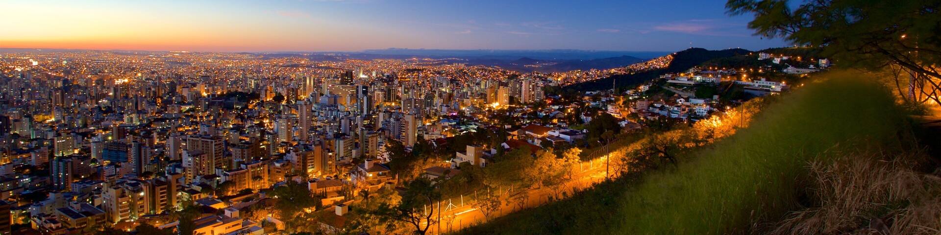 A cityscape at dusk with a view of the city lights and a hill in the foreground.