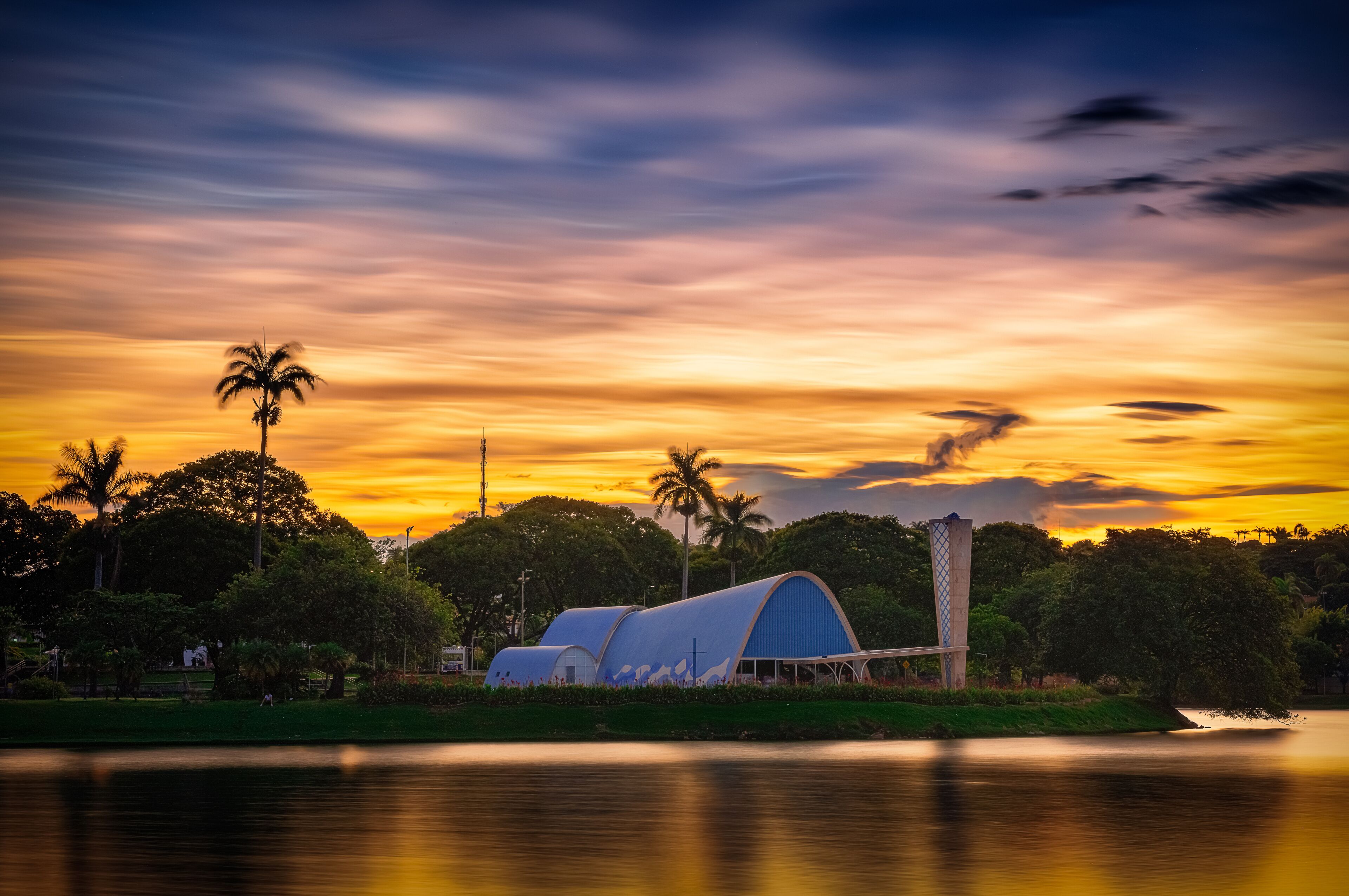 A sunset over a lake with a covered structure and palm trees.