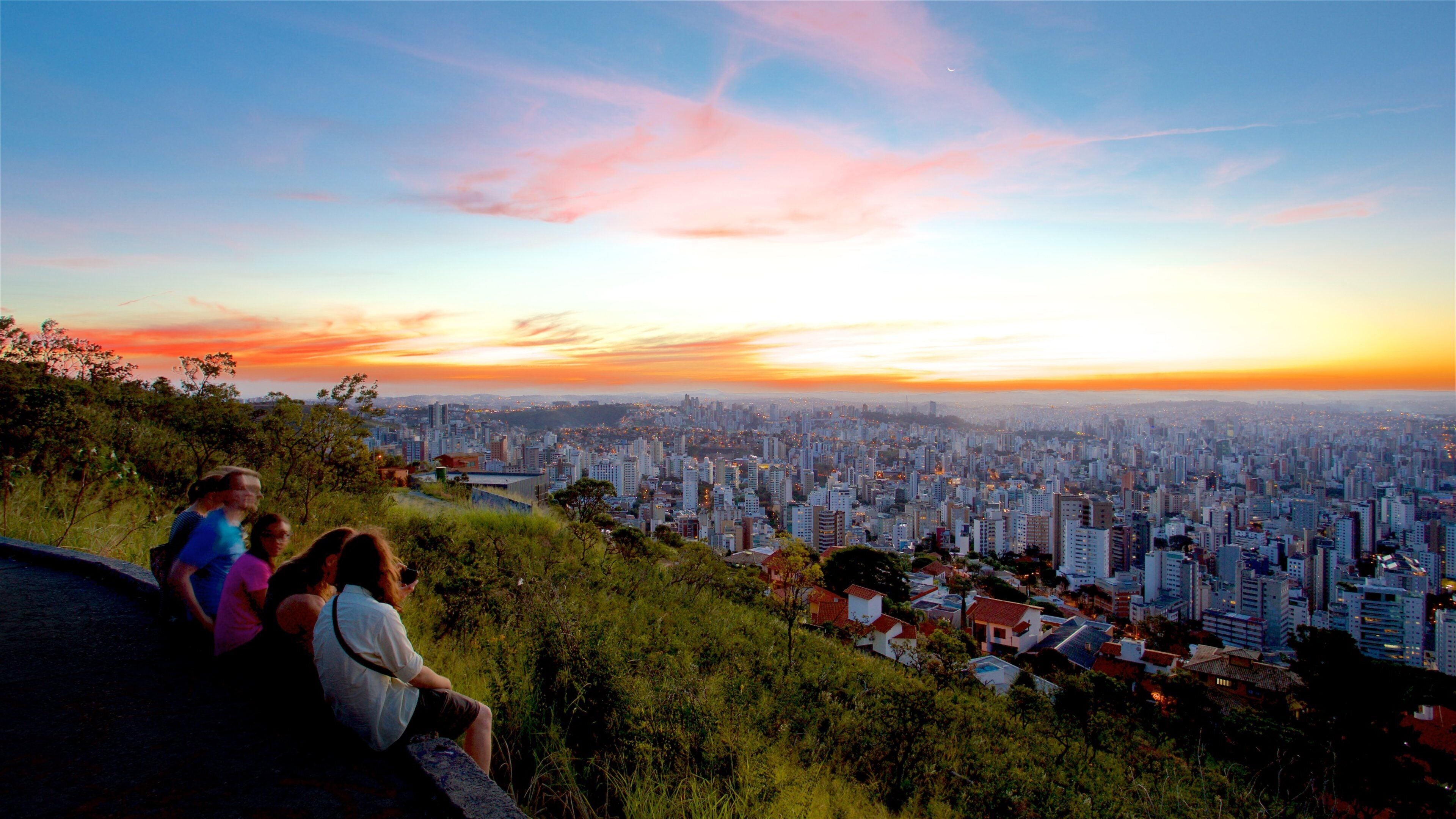 A cityscape at sunset with a view of the city from a hill.