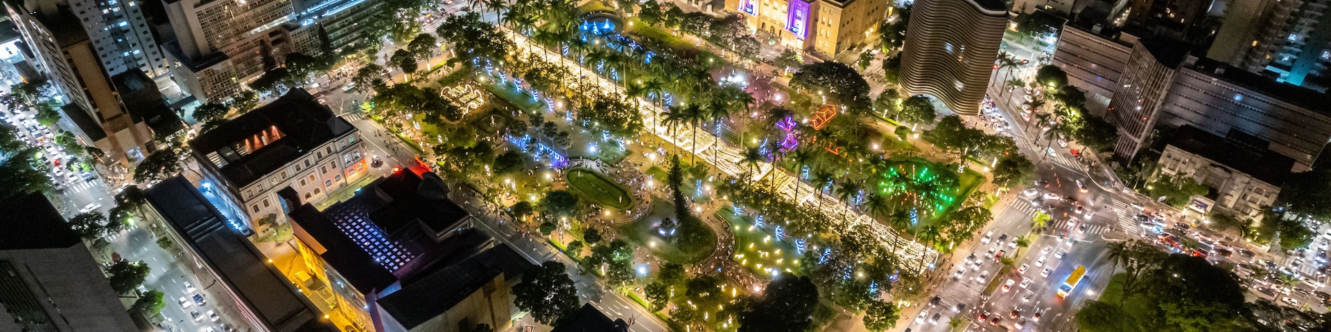 Luftaufnahme einer beleuchteten Stadt bei Nacht mit Straßen, Gebäuden und einem Park.