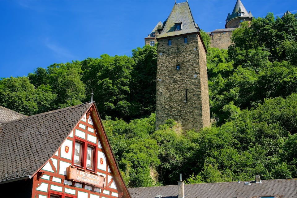 A traditional half-timbered house with a sign reading "Pension 23m Malerwinkel" in front of a castle with a tall tower on a hill.