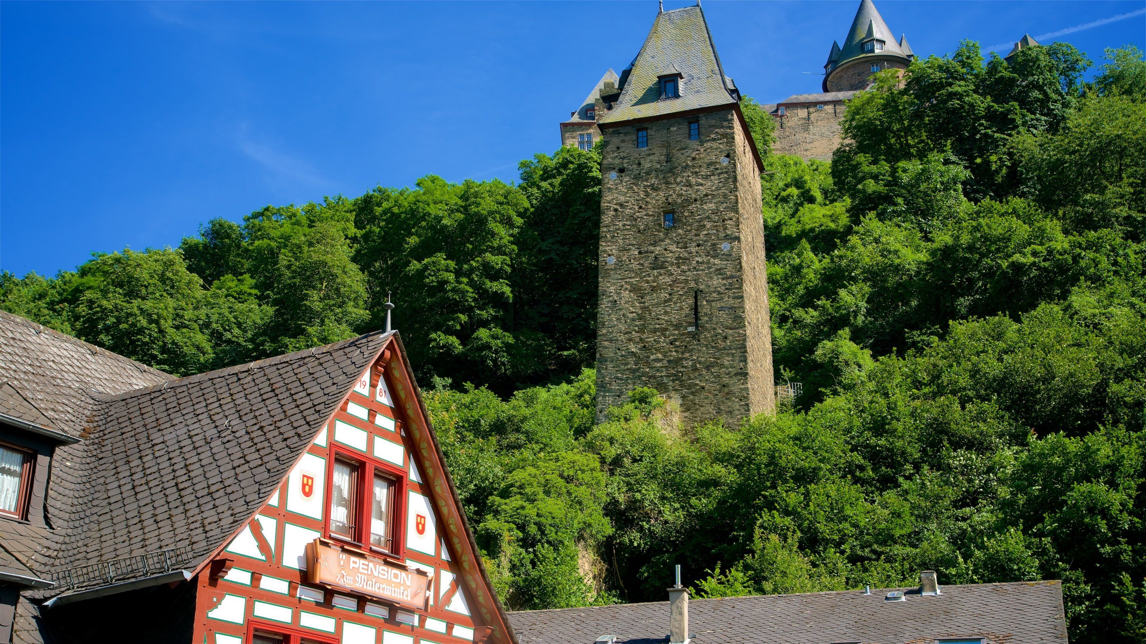 A traditional half-timbered house with a sign reading "Pension 23m Malerwinkel" in front of a castle with a tall tower on a hill.