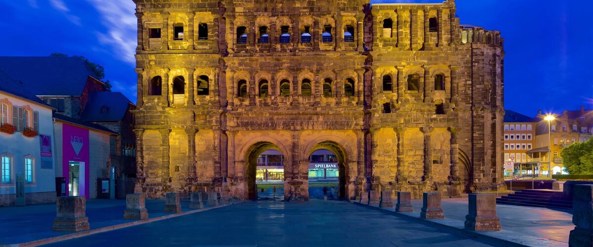 A historic stone building with multiple arches and a tower, illuminated at dusk.