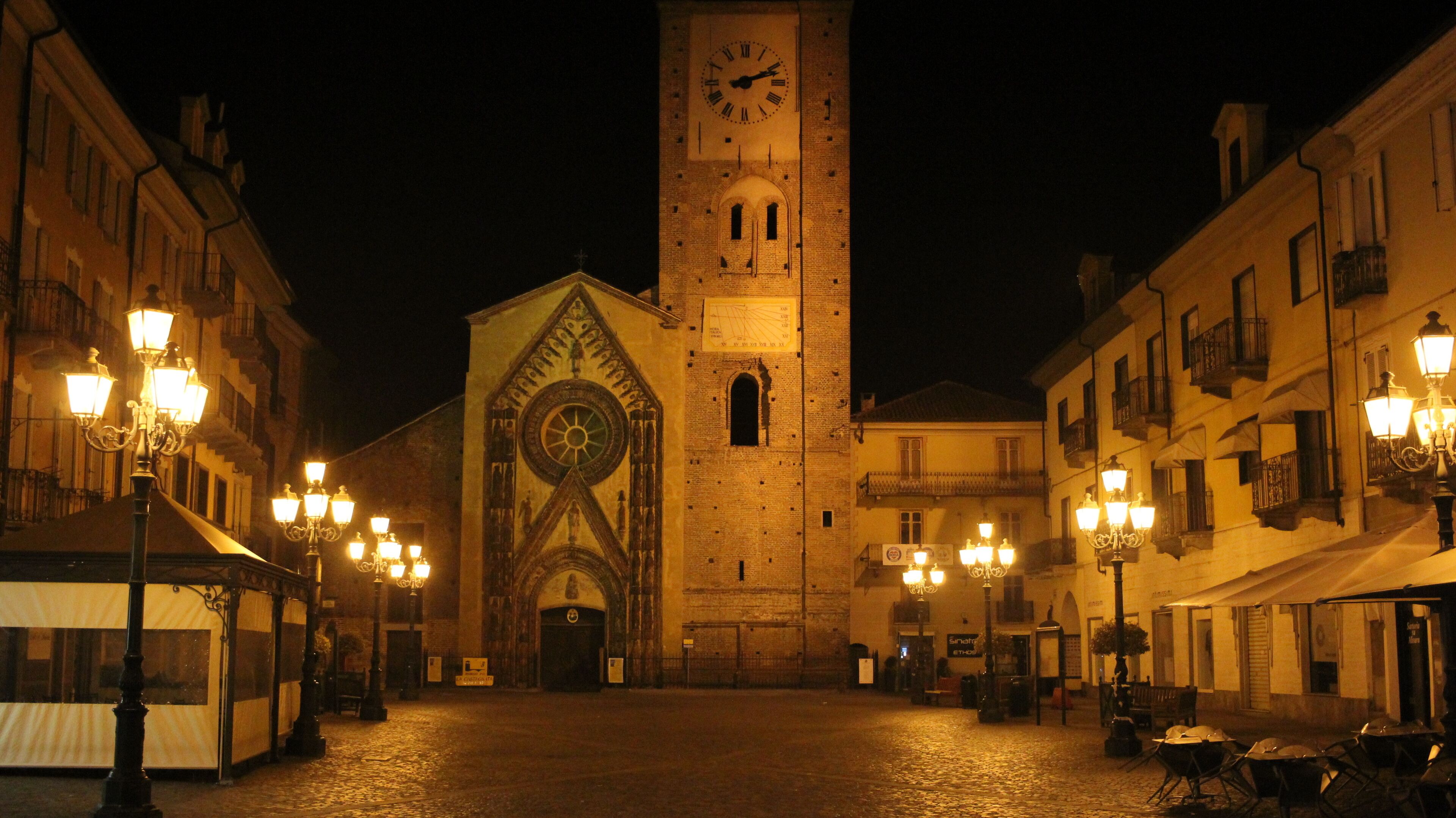 A historic square with a prominent clock tower, cobblestone streets, and ornate street lamps.