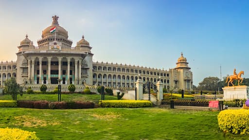 Panoramic view of Vidhana Soudha, the iconic government building in Bengaluru, India, captured during golden hour. The lush gardens and clear sky frame the historic architecture beautifully