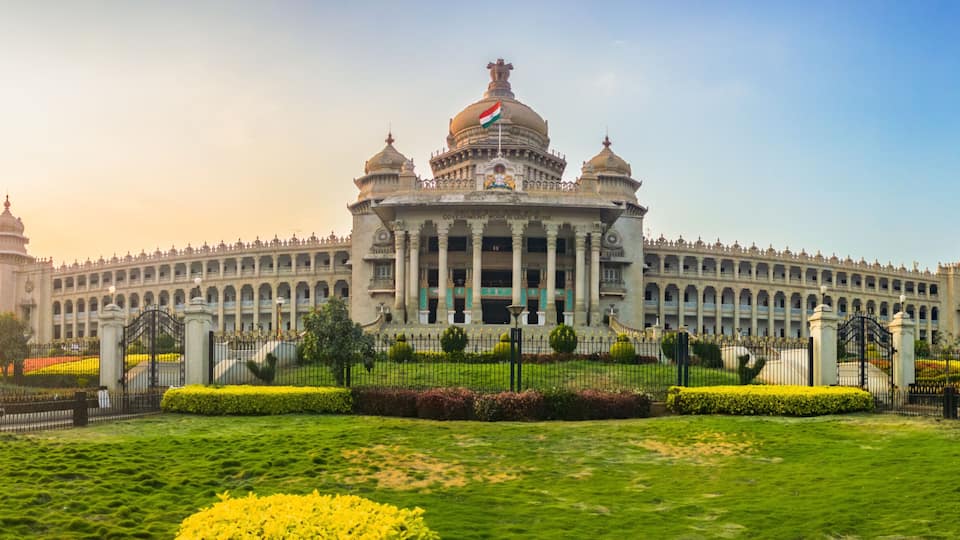 A large, ornate building with domed roofs and a central clock tower, surrounded by well-manicured gardens and statues.