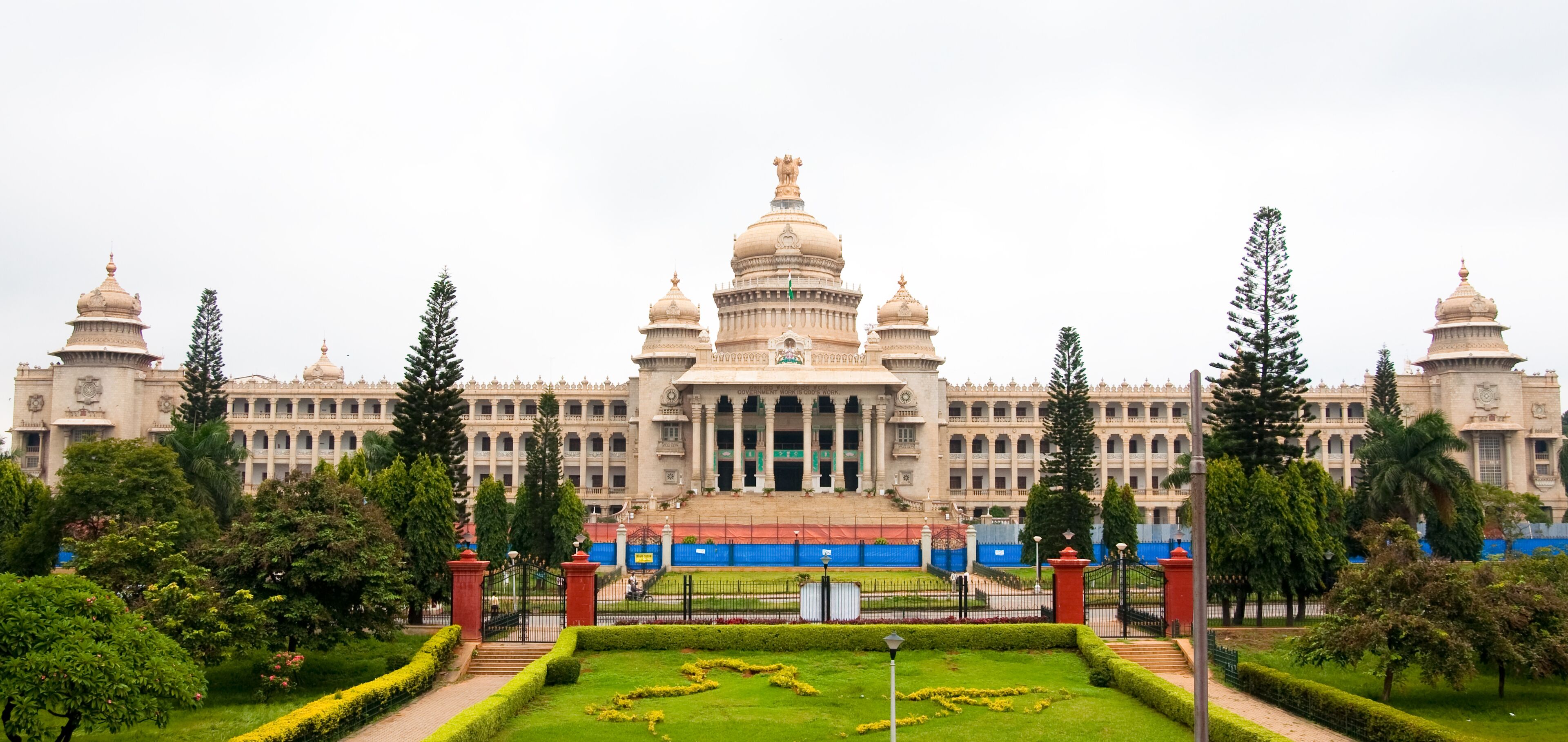 A large, ornate building with multiple domes and a central entrance, surrounded by well-manicured gardens and tall trees.