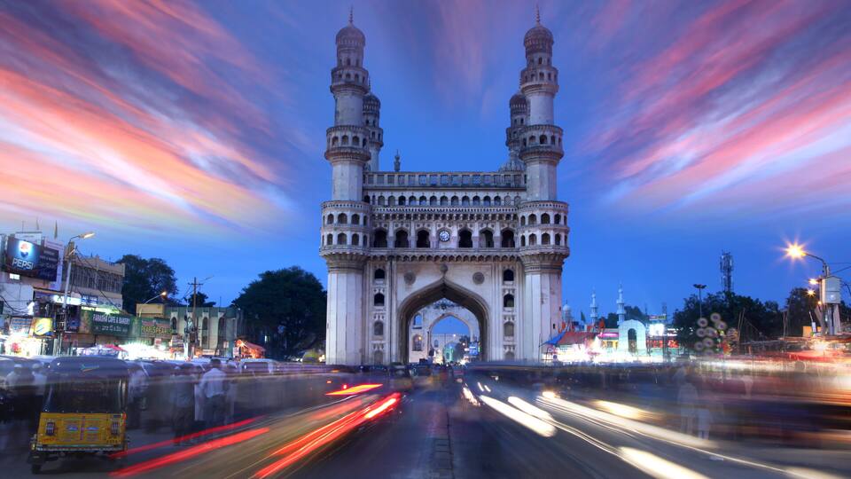 A historic archway with two towers, surrounded by a busy street at dusk.