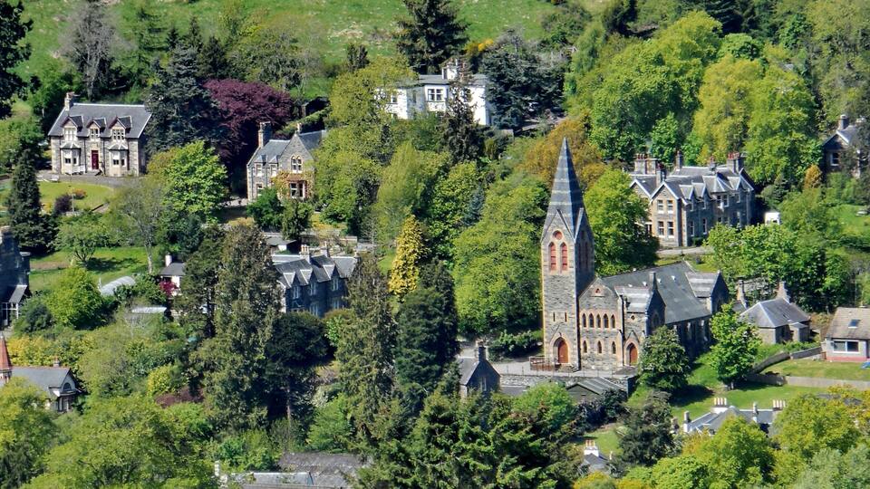 A village with historic stone buildings, a prominent church tower, and lush greenery.