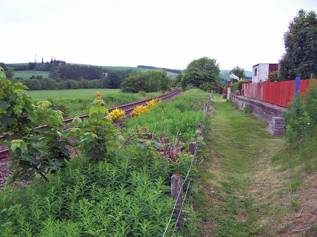 Site of Conon Bridge station. The railway is the Inverness to Wick and Thurso line, which opened in 1862. This photograph is taken from the end of Station Road, Conon Bridge. The station here closed in June 1960. What looks to be a former platform is on the right, and is now part of the back gardens of modern houses. If this was a platform - was there once a siding here? (See also File:Conon Bridge station (former) - geograph.org.uk - 1925307.jpg ). Update: I have been contacted by Alasdair Cameron, who confirms "Yes, there were several sidings and a large goods shed". Thank you for the information Mr Cameron.