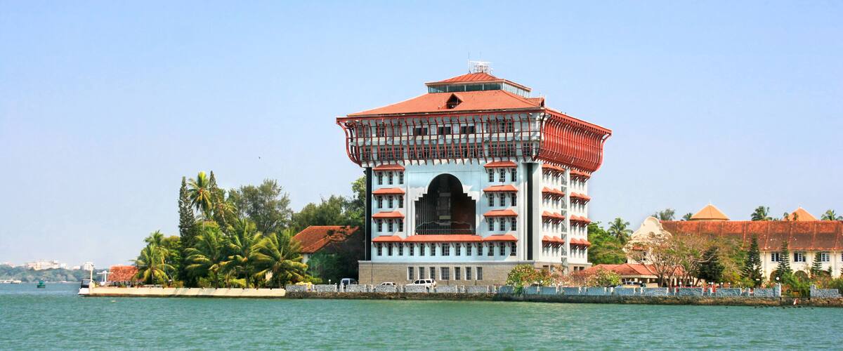 A large, multi-story building with a red roof and white walls, situated by a body of water.
