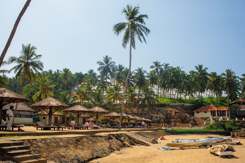 A beach with thatched umbrellas, palm trees, and a sandy shore with boats.