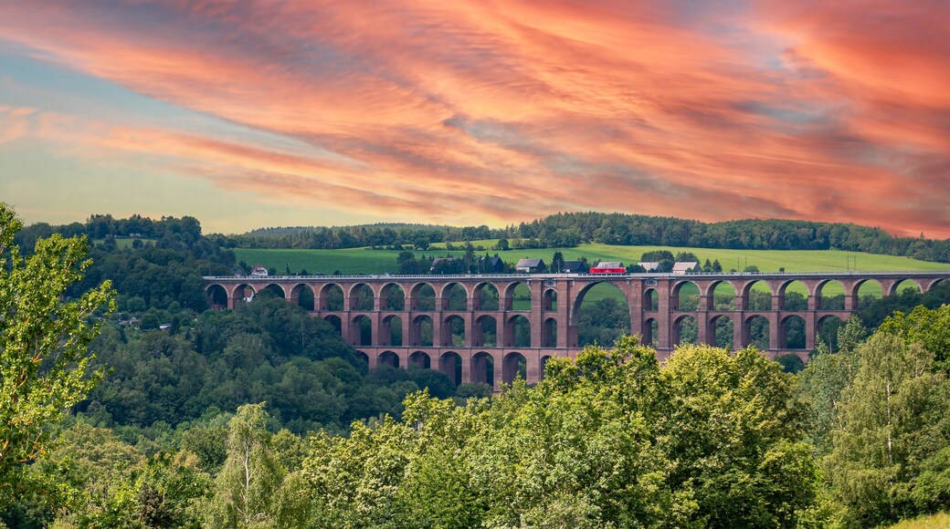 Un largo viaducto cruza un valle, rodeado de colinas verdes y un cielo con un atardecer espectacular.