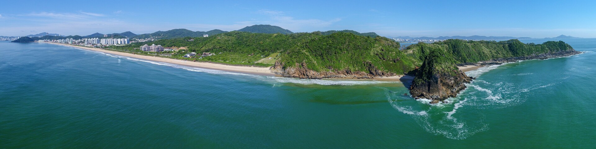 A coastal landscape with a beach, a forested island, and a cityscape in the background.