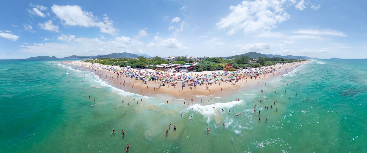 A tropical beach with clear turquoise waters, a sandy shore, and a small island with buildings and greenery in the background.