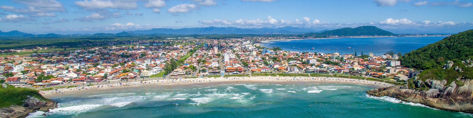 Uma cidade costeira com praia, oceano e montanhas ao fundo.