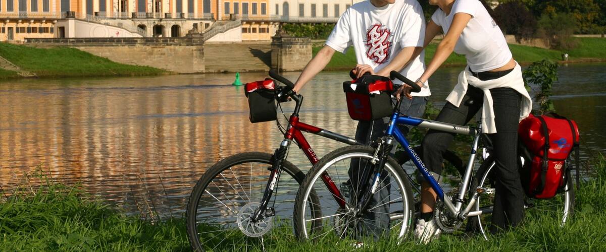 A couple standing by a river with a historic building in the background.